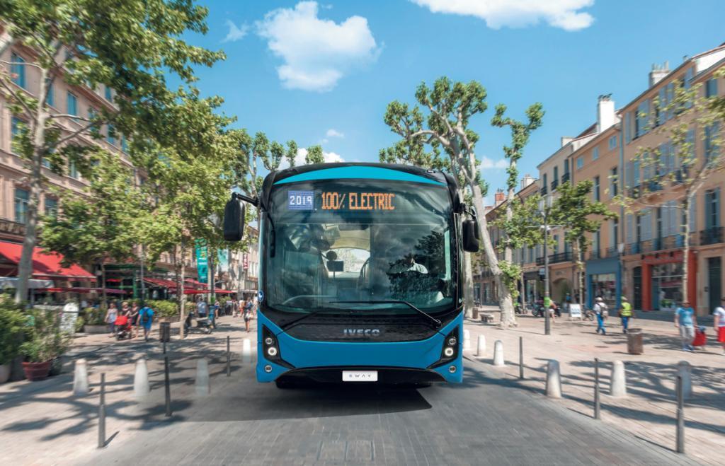 Ein blauer IVECO Bus E-Way fährt mit der Aufschrift 100% electric in einer Fußgängerzone.