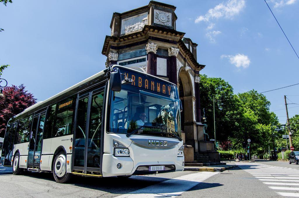 Ein weißer IVECO Bus Urbanway steht in der Innenstadt vor einem historischen Torbogen.