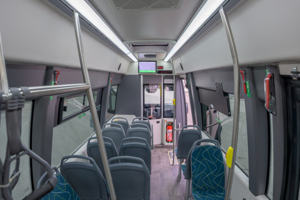 Der Innenraum vom Iveco Daily Access zeigt links zwei und rechts eine Sitzreihe. Der Fahrer ist in einer Kabine vom Innenraum abgetrennt und davor ist ein Feuerlöscher in einem Schrank montiert.